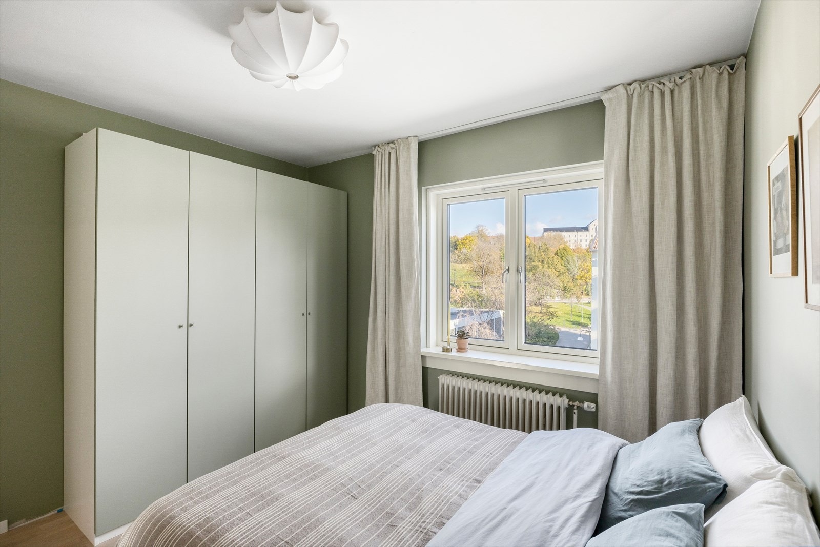 Garderobeløsning som utnytter veggflaten godt og gir ryddig oppbevaring av klær og sko. Her kan man nyte en kaffe på sengen mens man ser utover i Tøyenparken Galleribilde