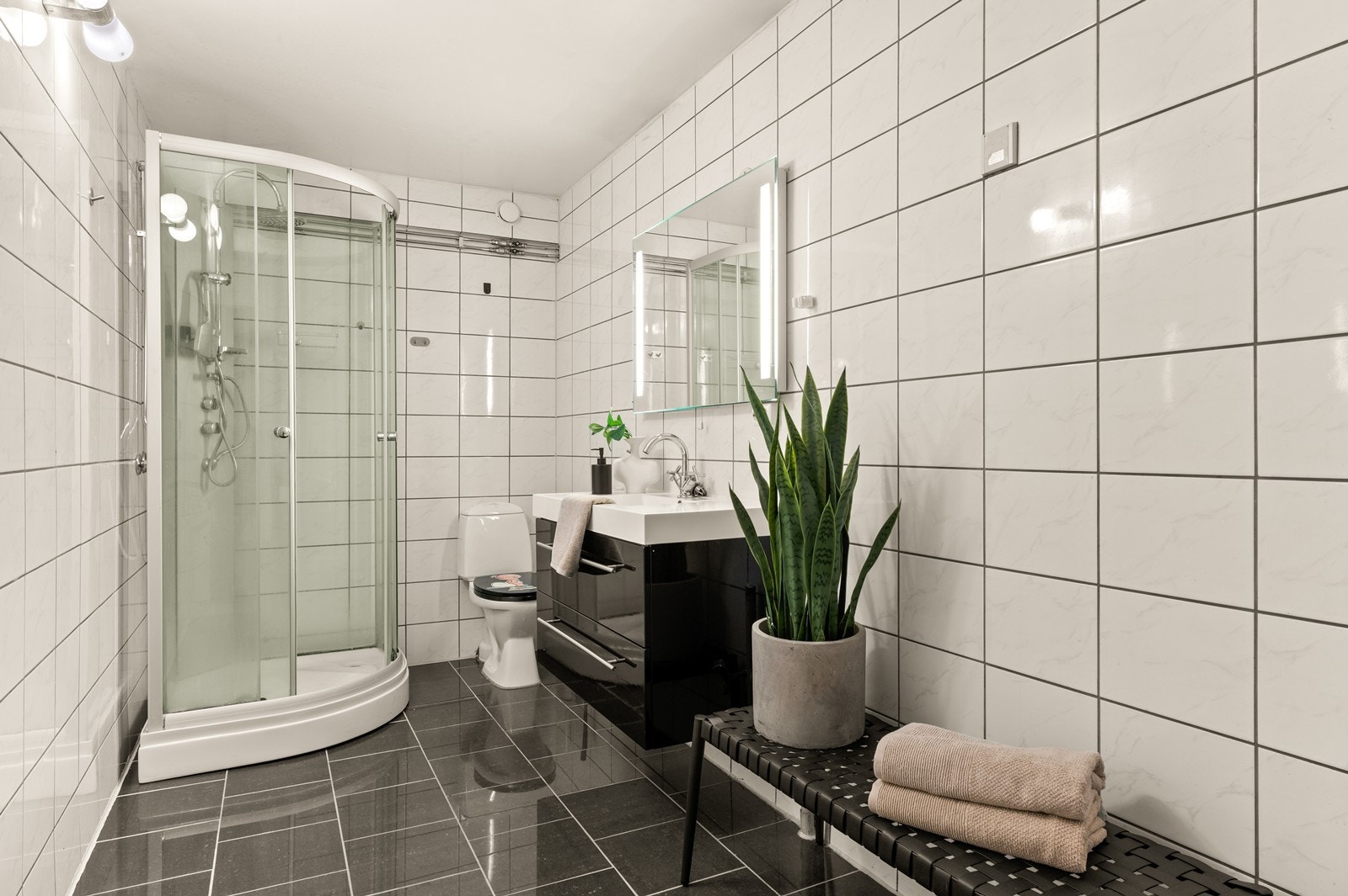 Badet ble modernisert rundt 2011 og er helfliset, og rommet er utstyrt med dusjkabinett og moderne servantinnredning, med lagringsplass i skjuffene. Over servanten er det speil med ledlys. I tillegg er det gulvmontert wc. Galleribilde