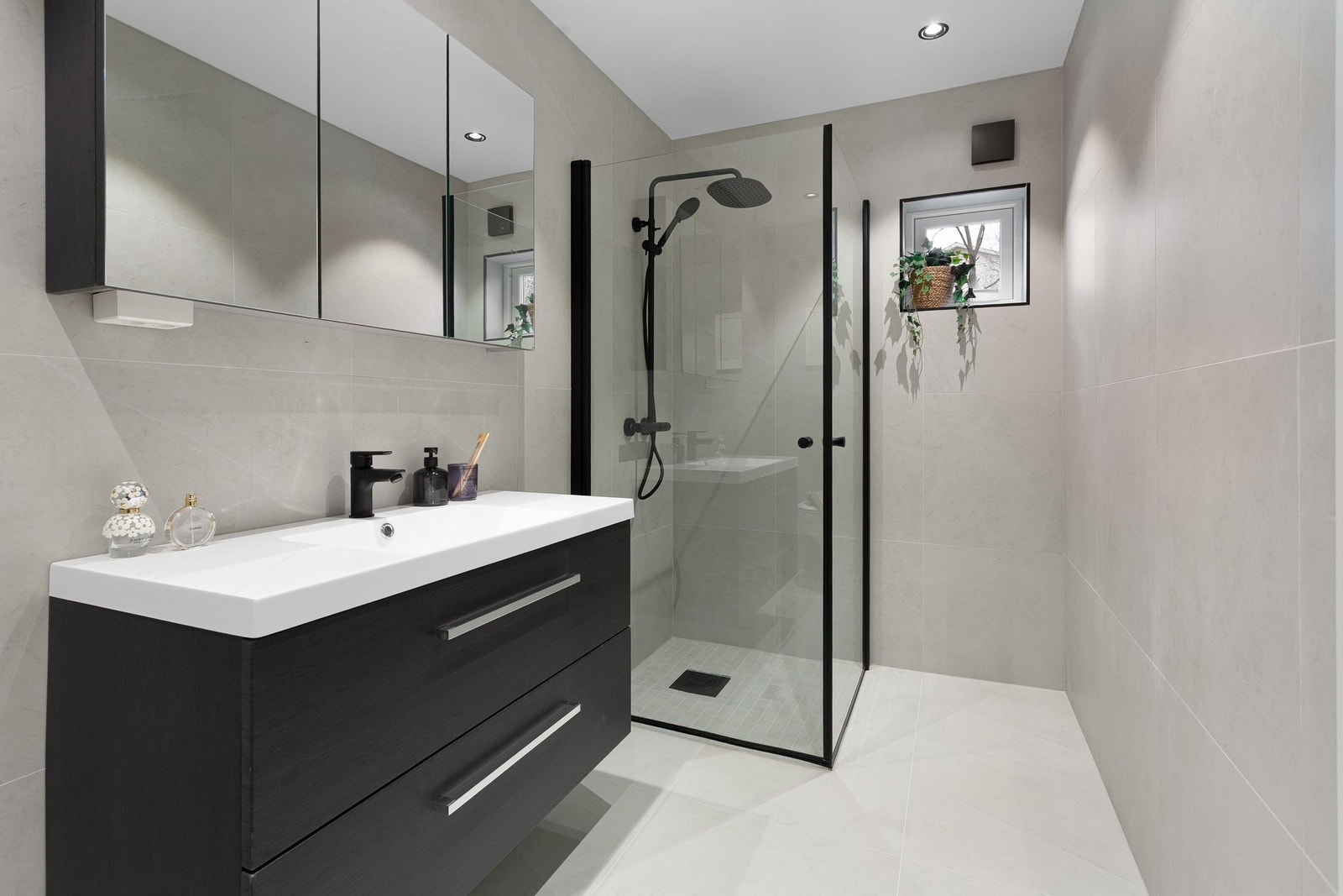 Stilrent bad med tidsriktige 60X60 fliser på gulv med varmekabler og dimbare downlights i tak Galleribilde