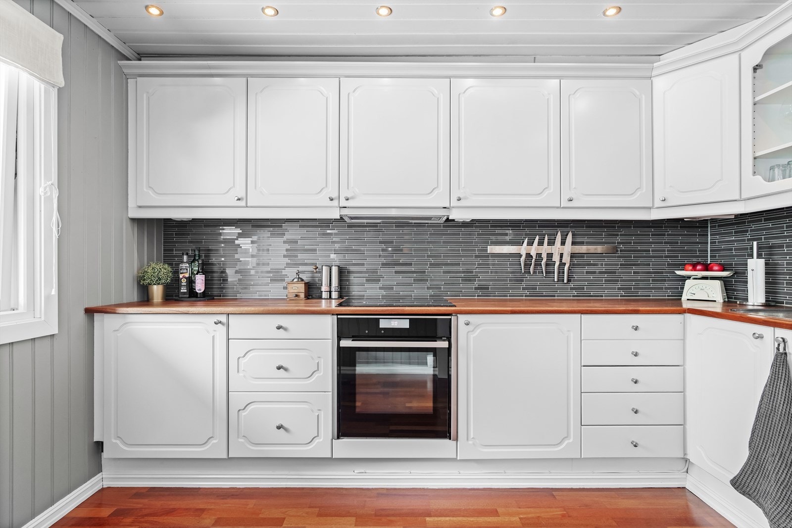 Det er lyse, profilerte fronter og heltre benkeplate, samt moderne fliser mellom benkeplate og overskap. Galleribilde