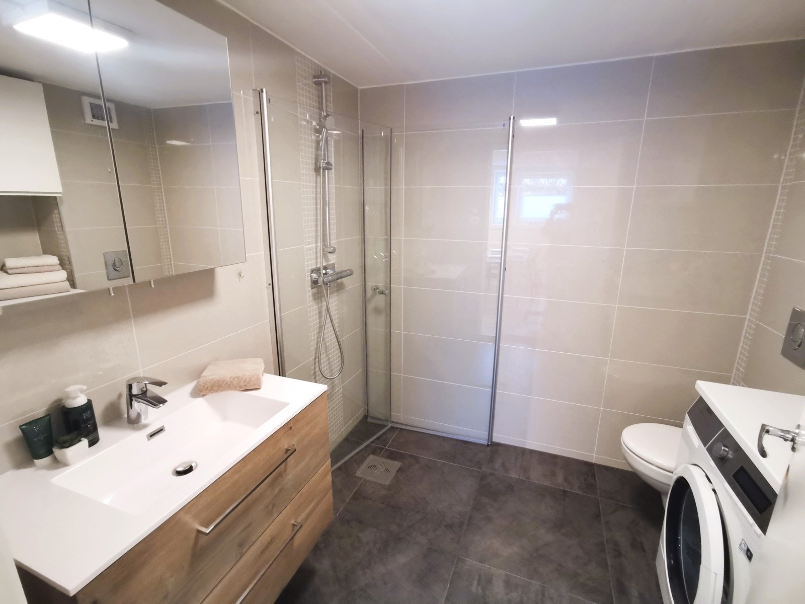 Lekkert flislagt bad pusset opp i 2025, med grå fliser på gulvet og lyse fliser på veggene som gir et moderne og rent uttrykk. Galleribilde