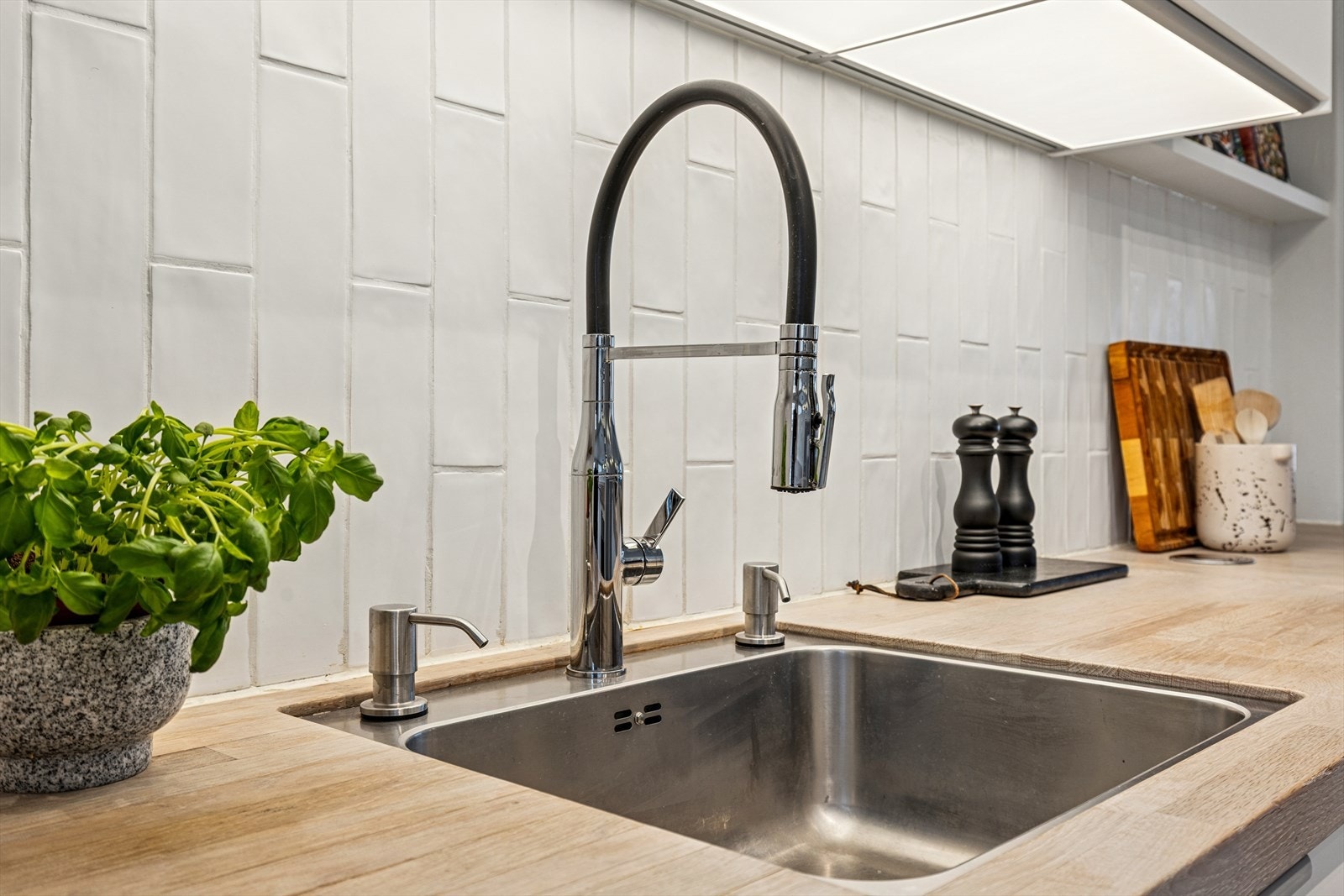 Detalj fra kjøkkenet med moderne armatur, nedfelt vask og stilrene fliser som gir et helhetlig og tidløst uttrykk Galleribilde