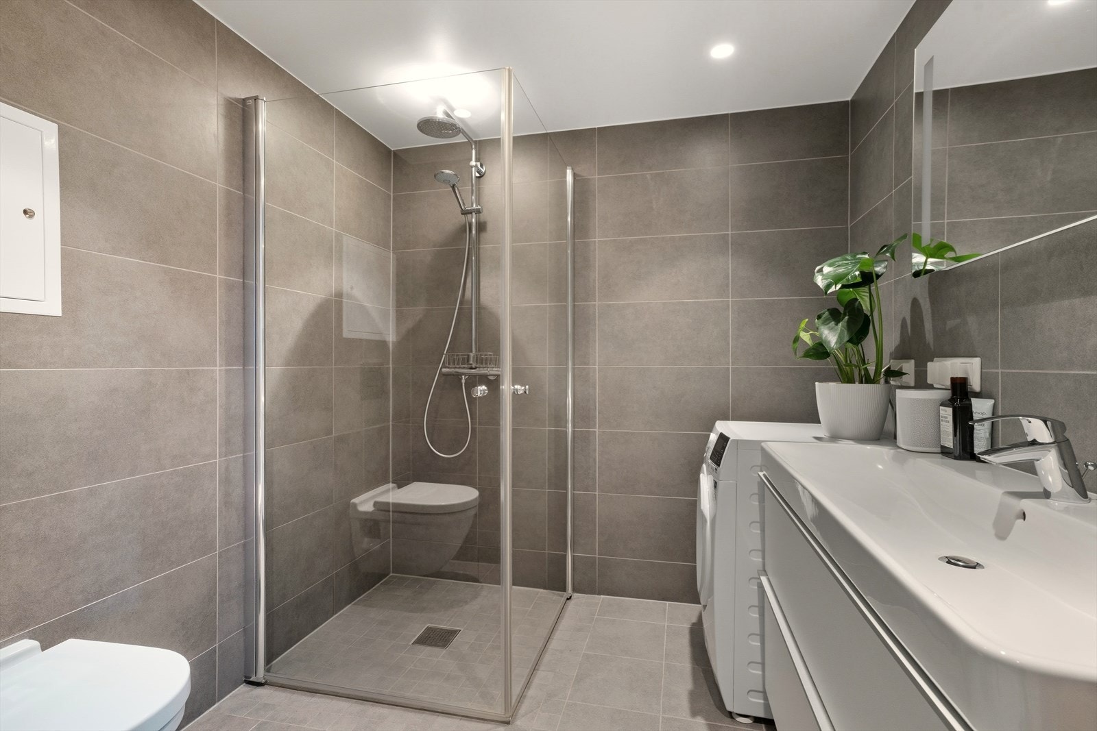 Badet har flislagt gulv og vegger i en moderne gråtone, og det er elektrisk gulvvarme. Galleribilde