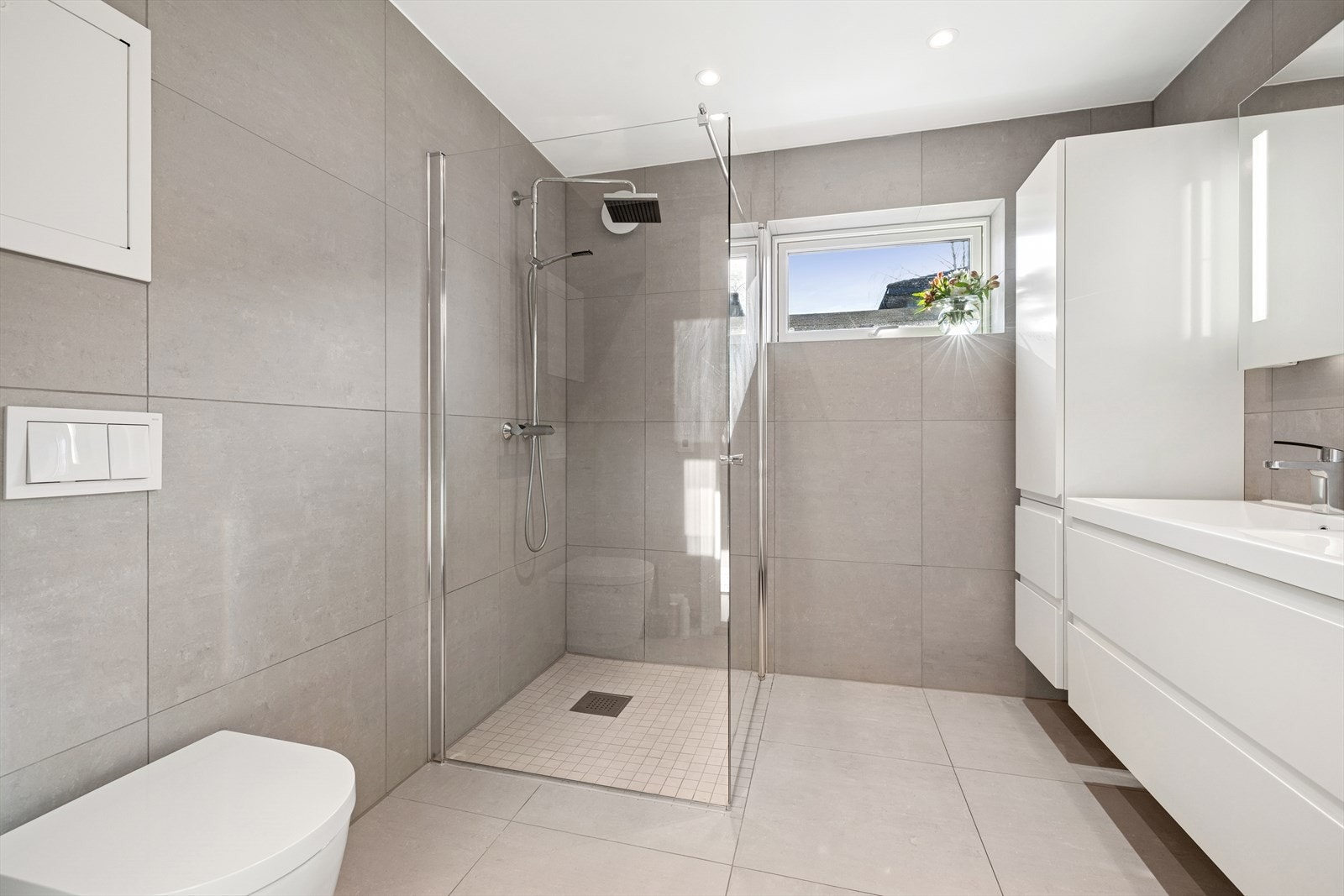 Badet har fliser på vegger og gulv med gulvvarme. Badet har innredning med 2 nedfelte servanter, veggmontert toalett og dusjhjørne. Galleribilde