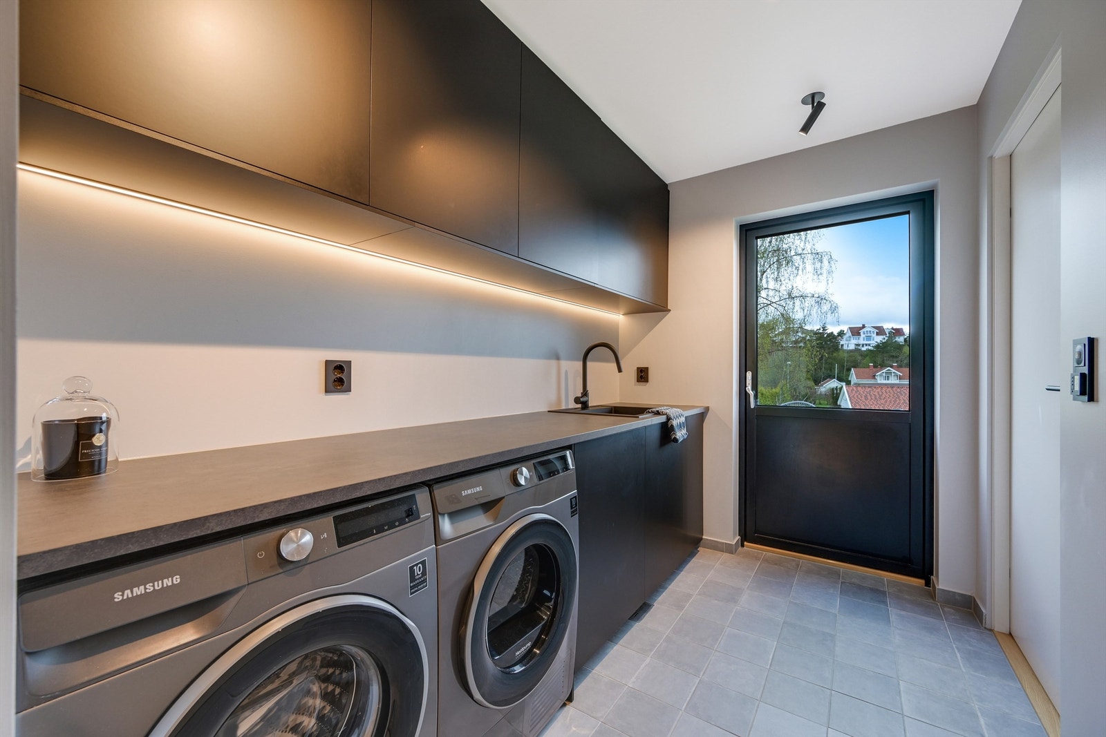 Praktisk vaskerom med før ut til baksiden av tomten med en stor platting/uteplass Galleribilde