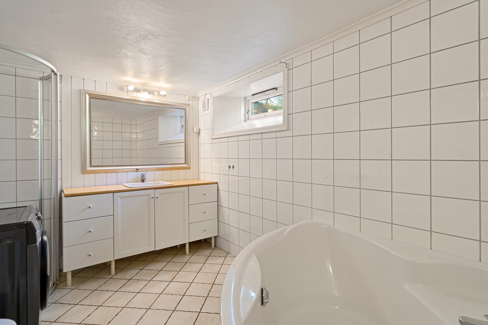 Flislagt bad med badekar, dusj, servant med skap og toalett Galleribilde