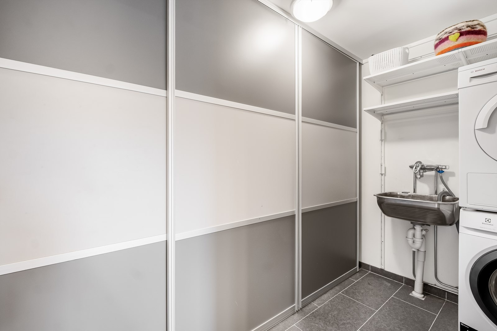 Vaskerom med flislagt gulv og varmekabler. Praktisk skyvedørsgarderobe og opplegg til vaskemaskin. Galleribilde