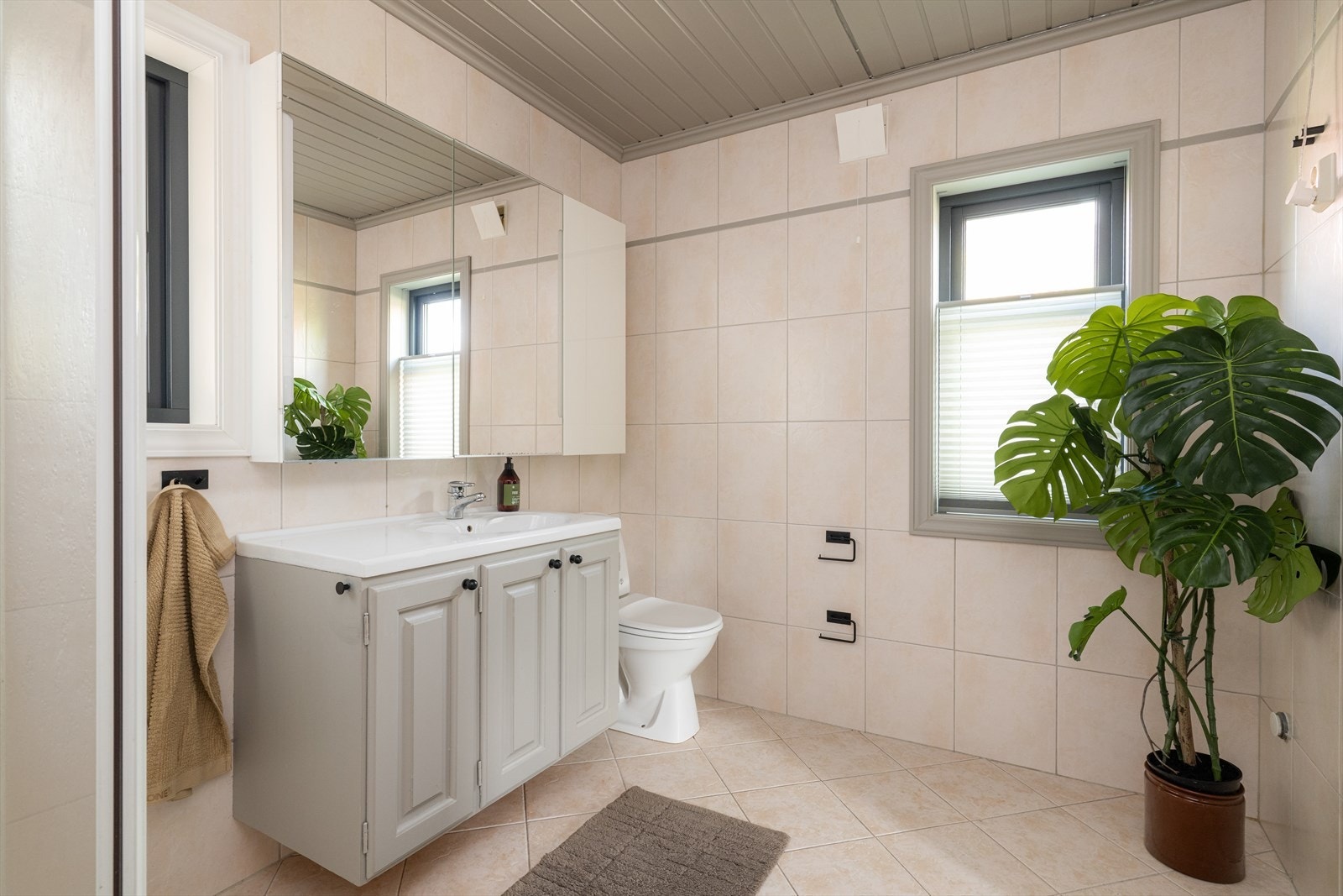 Boligen har helfliset bad i duse fargetoner med sorte detaljer i dusjgarnityr og tilbehør. Badet har innredning med heldekkende servant og stort speilskap. Galleribilde