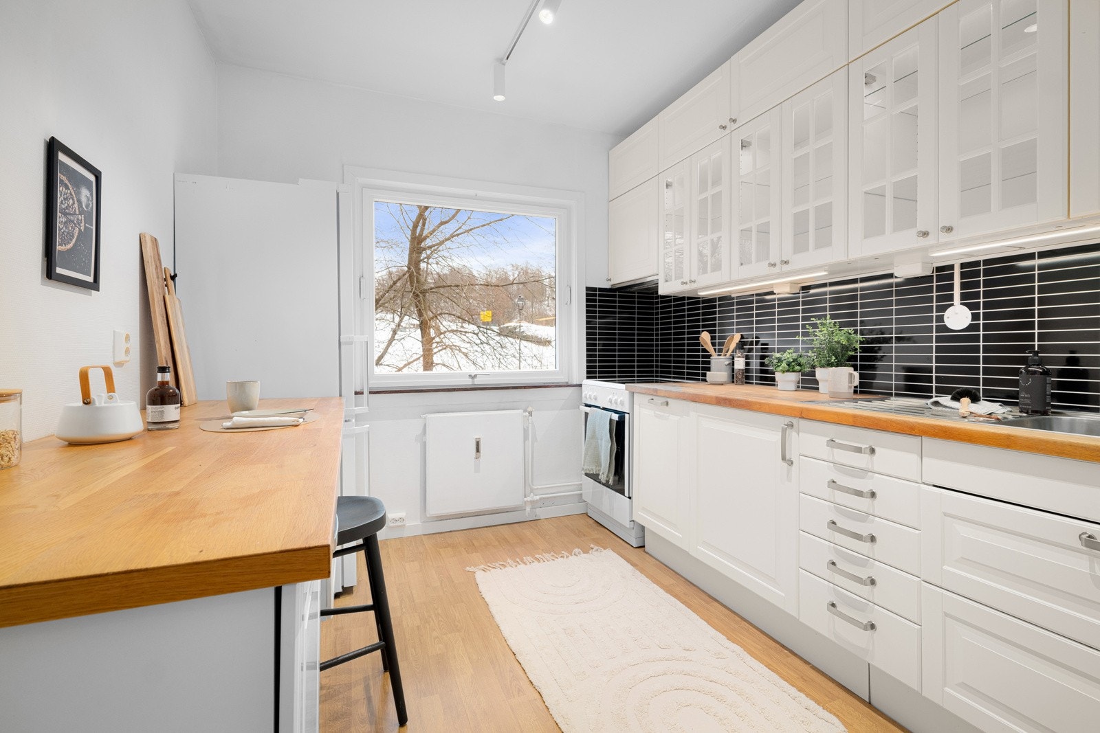 Innredningen har lyse profilerte fronter og benkeplater av treverk med nedfelt dobbel oppvaskkum. Praktisk med flisimitasjonsplater i benkeryggen og belysning under overskapene. Galleribilde