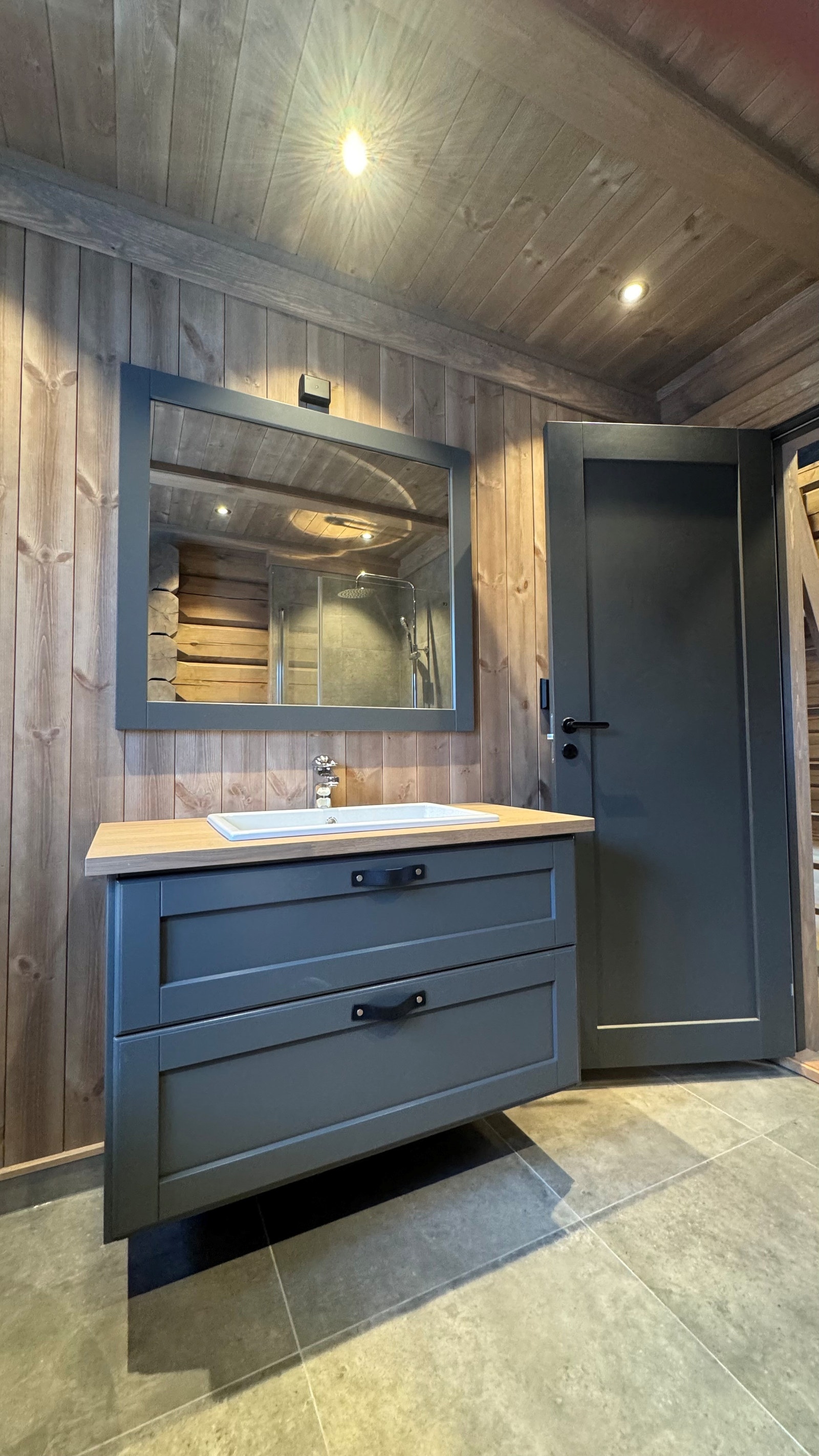 Hytta har et delikat og fullt utstyrt bad. Badet er utført med moderne, grå fliser på gulv, og flis i dusj-sone forøvrig tømmer på vegg. Baderomsinnredning fra Kistefos. Galleribilde