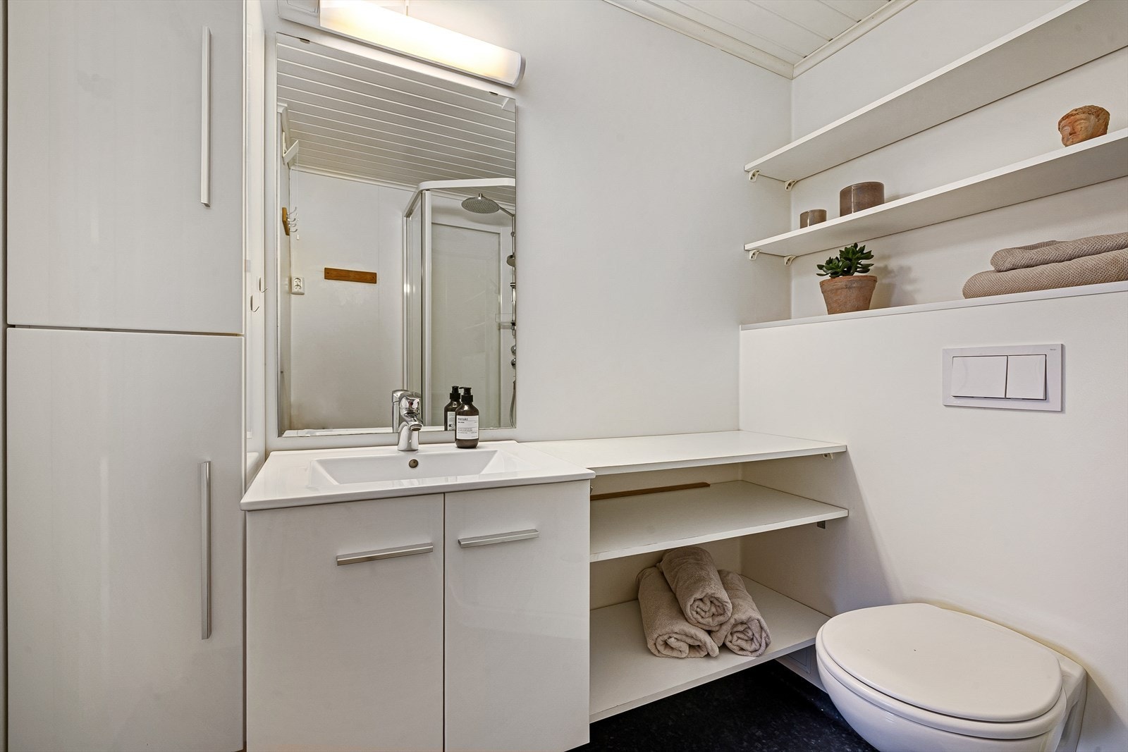 Badet er utstyrt med vegghengt toalett, innredning med servant og hyller, dusjkabinett og opplegg til vaskemaskin. Galleribilde