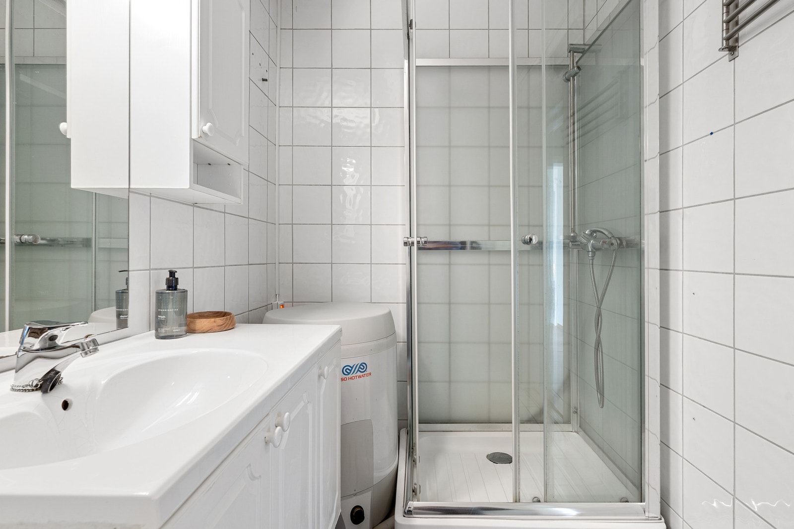 Badet er innredet med veggmontert servant og skapinnredning med speil, dusjkabinett Galleribilde