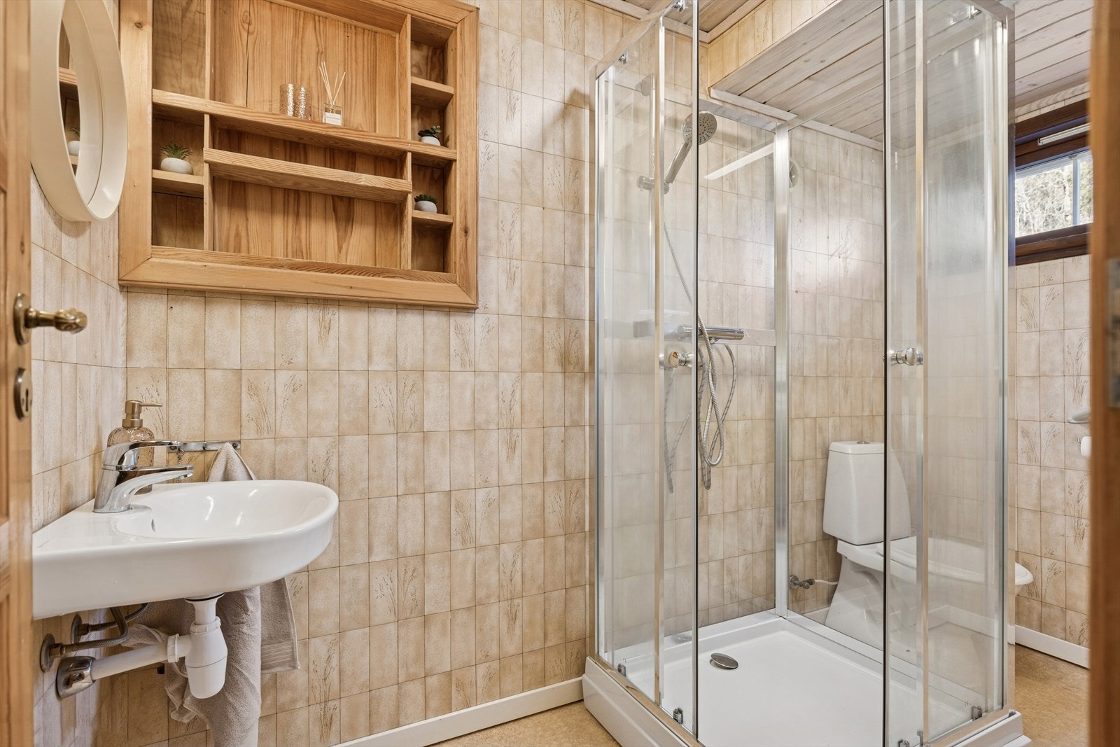 Enkelt baderom med gulvstående toalett, servant og dusjkabinett. Galleribilde