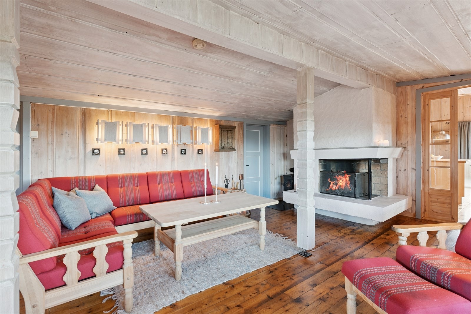 Den hvitmalte peisen er plassbygd, og fungerer som et eget, fint møbel i stua. Nær peisen er det vedovn som også gir lun og god varme. Galleribilde