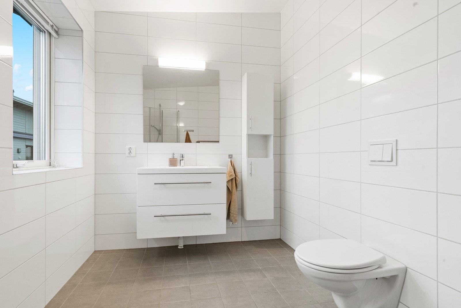 Baderommet har vegghengt toalett, dusjløsning og servant på skuffeseksjon. Galleribilde