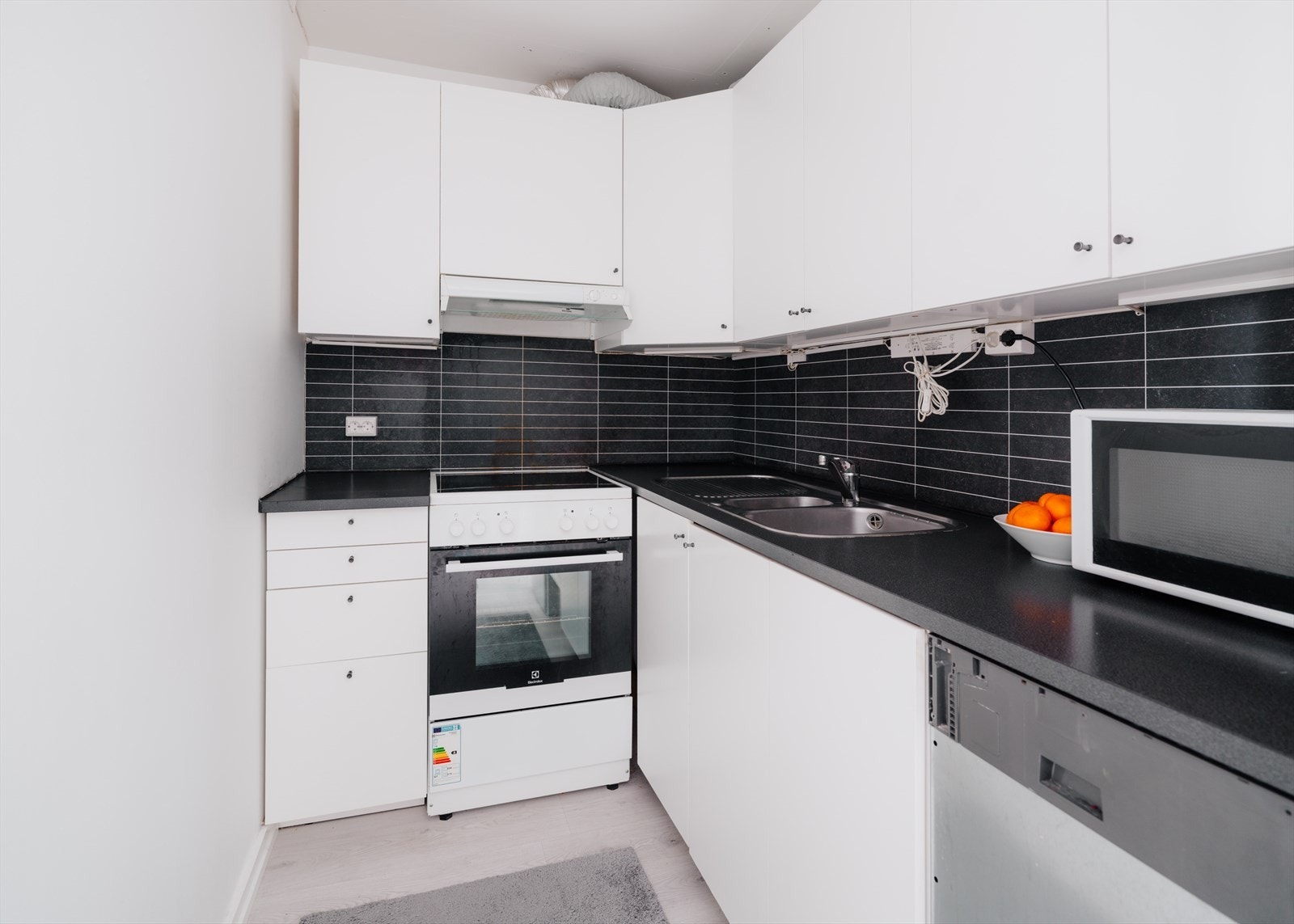 Kjøkkeninnredning med glatte fronter, belysning under overskap og praktiske plater på vegg over benkeskap. Laminert benkeplate med nedfelt kum i rustfritt stål Galleribilde