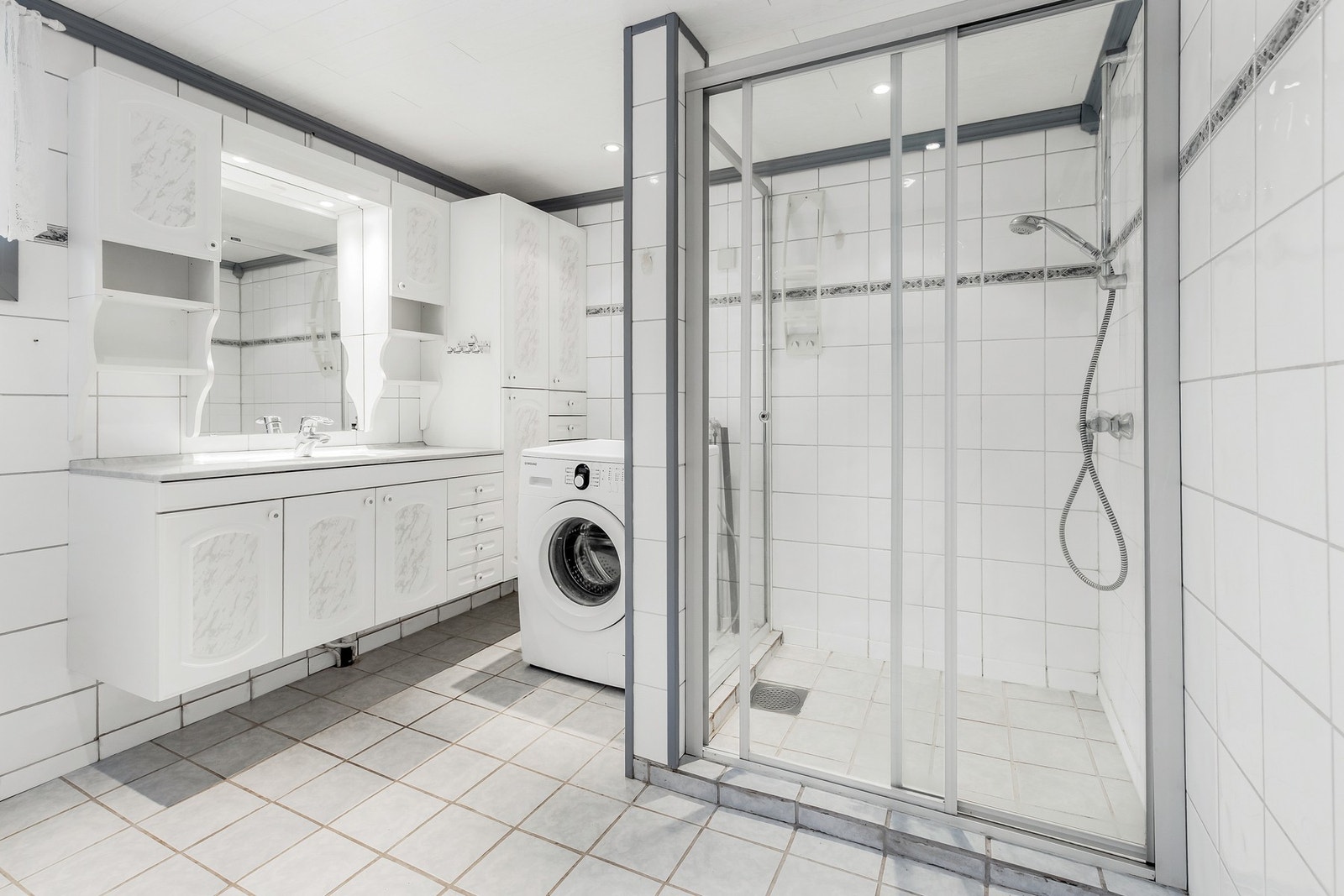 Rommet er innredet med dusjhjørne, servant i innredning, gulvstående toalett og opplegg for vaskemaskin Galleribilde
