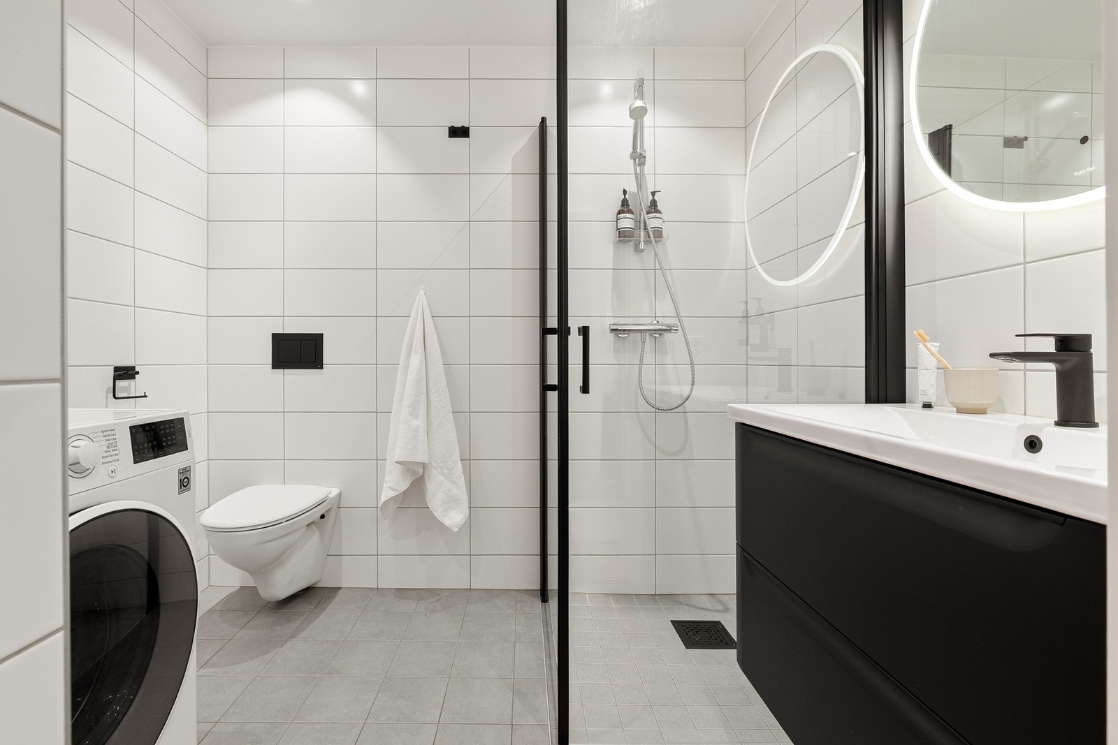 Badet er praktisk innredet med veggmontert toalett, dusjhjørne, skuffeseksjon med overliggende servant, opplegg for vaskemaskin. Galleribilde