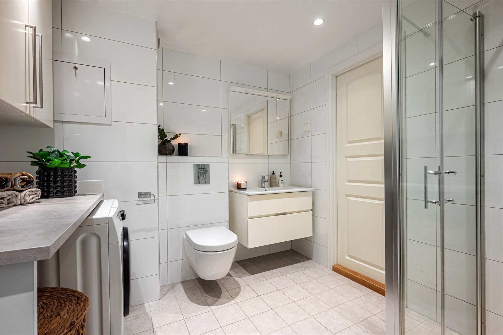 Flislagt og pent bad innredet med vegghengt toalett, dusj med glassvegger og servantinnredning med god oppbevaring. Her er det også opplegg for vaskemaskin og tørketrommel i en praktisk innredning med oppbevaring og benkeplass. Galleribilde