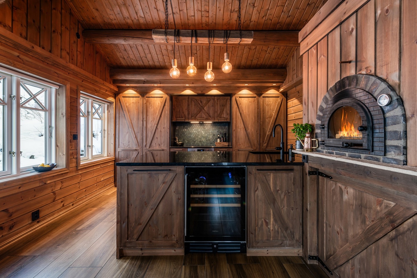 Stilig, plassbygd kjøkkeninnredning med over- og underskap med fronter i heltre og benkeplate i granitt med underlimt kum og blandebatteri med Quooker Galleribilde