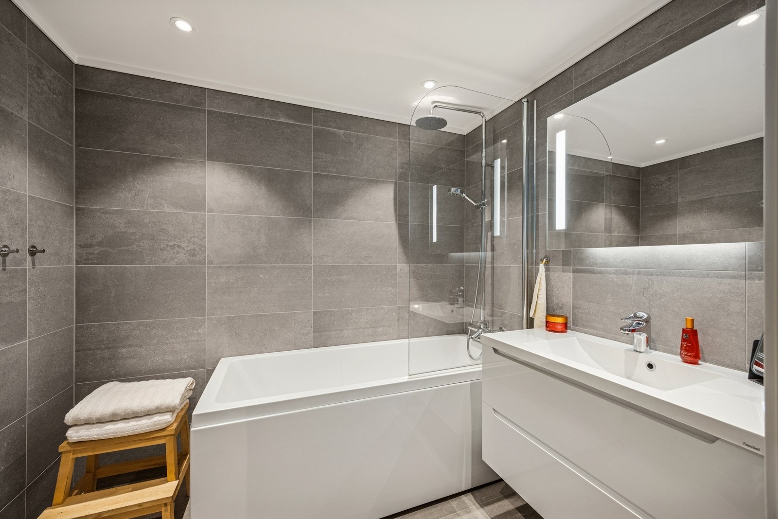 Flislagt bad med nedfelt servant, veggmontert toalett og badekar. Galleribilde