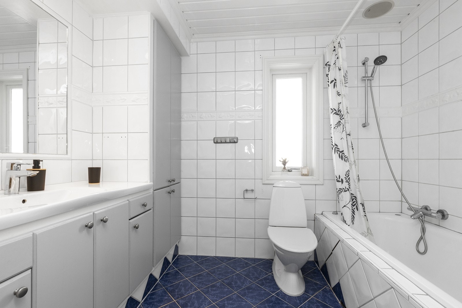 Bad/wc fra byggeår med fliser på gulv med gulvvarme, fliser på vegg og malt panel i tak Galleribilde