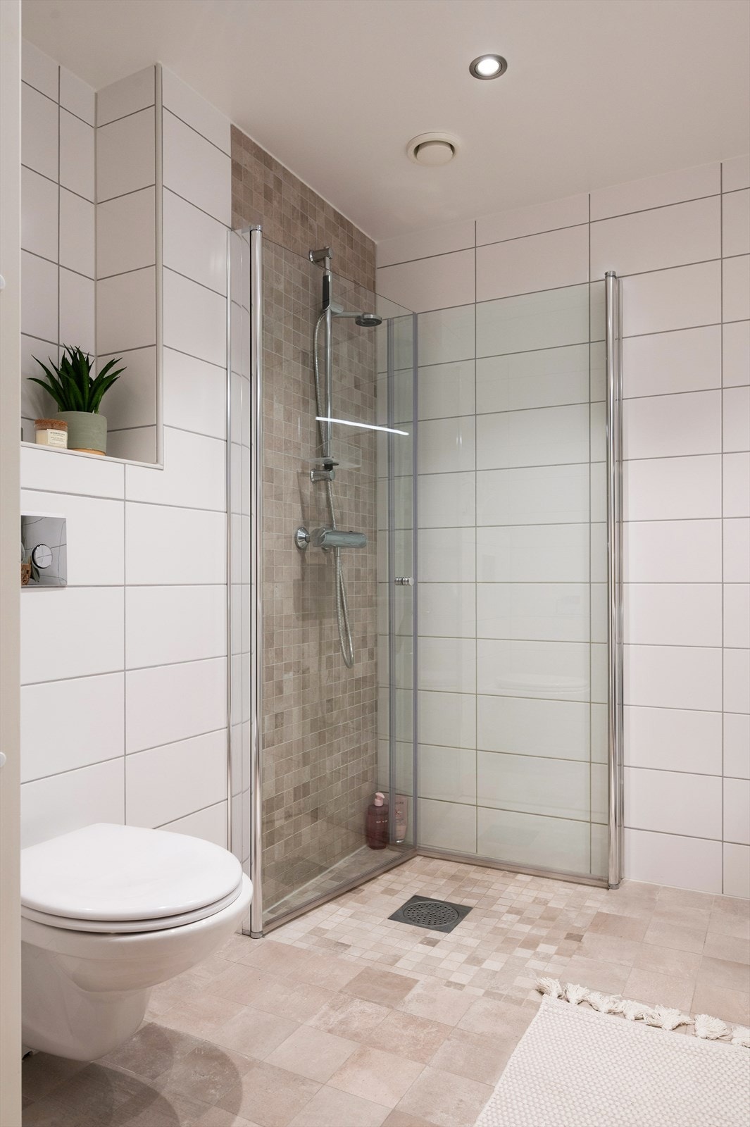 Badet er utstyrt med vegghengt toalett og dusjhjørne med innfellbare dører i herdet glass Galleribilde