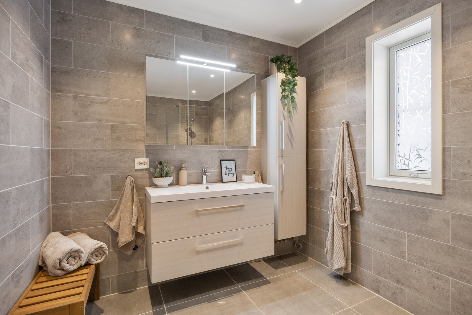 Badet har delikate farge- og materialvalg og lun atmosfære. Her er det downlights i himlingen, grå fliser på veggene og matchende fliser på gulv med gulvvarme. Galleribilde