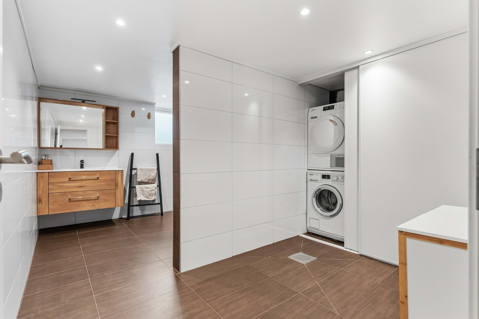 Badet i kjelleretasjen har praktisk løsning med vaskemaskin og tørketrommel gjemt bak en skyvedørsskap. Galleribilde