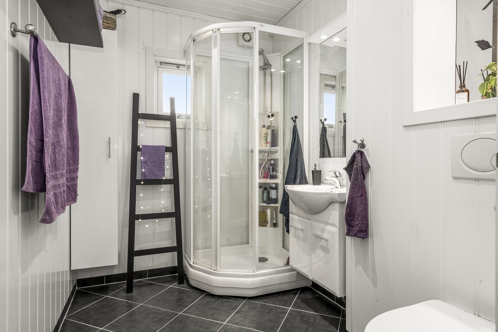 Flislagt gulv og mdf-panel på vegger gir et stilrent bad med dusjkabinett og vegghengt toalett. Galleribilde