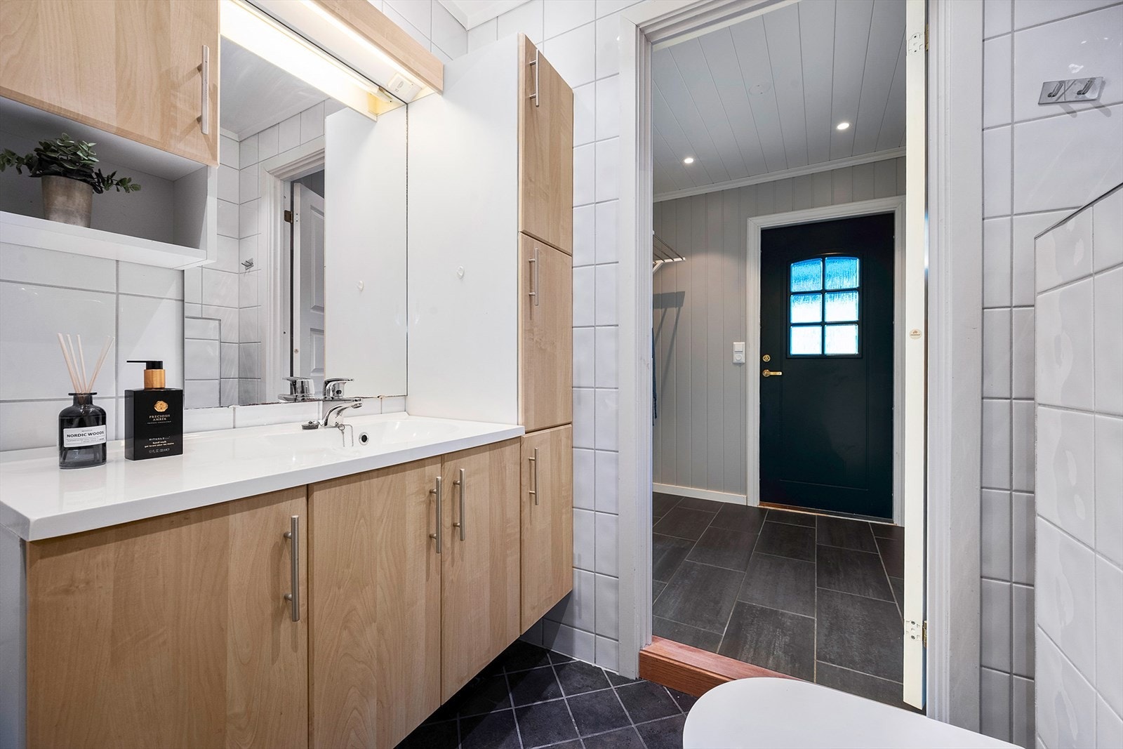 Badet er innredet med veggfestet WC, dusjbatteri med innfellbare dusjvegger og baderomsinnredning med speil og heldekkende servant. Galleribilde