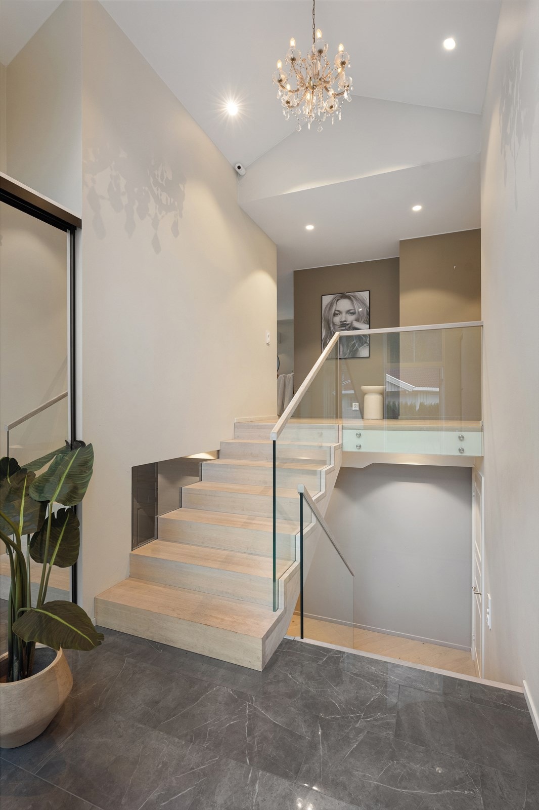 En stilren trapp med eiketrinn og glassrekkverk leder elegant ned til underetasjen. Galleribilde