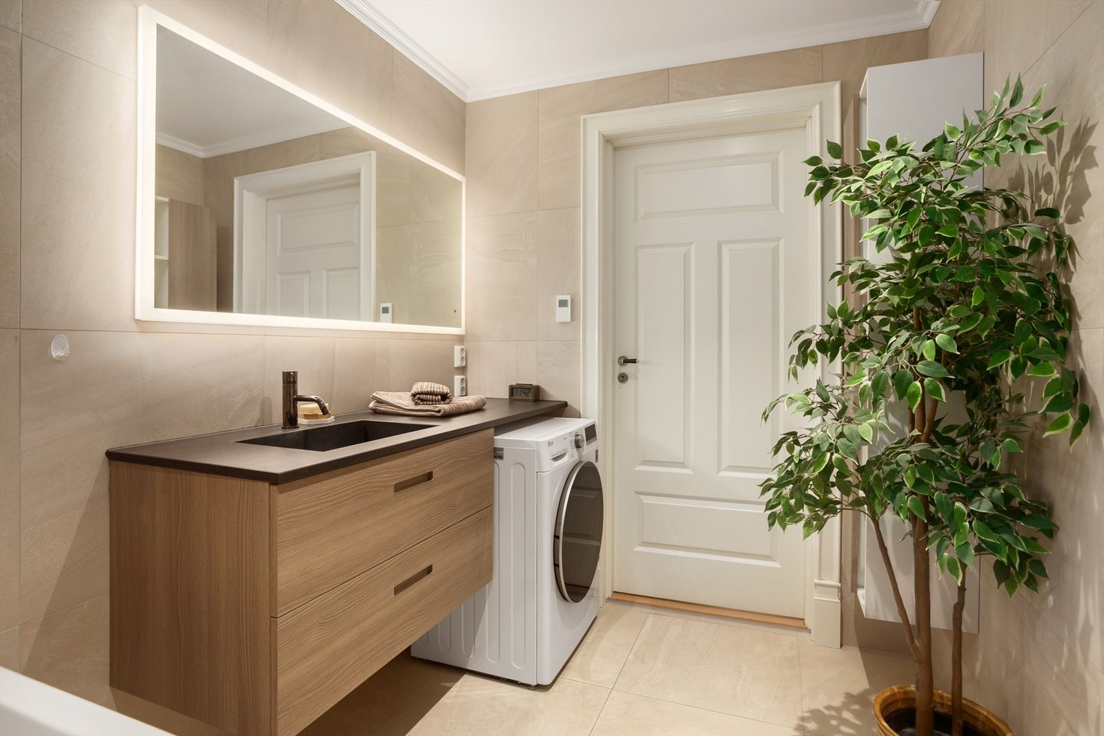 Badet er utstyrt med heldekkende servant med underskap og nisje for vaskemaskin, badekar og dusjarmatur, vegghengt skap og toalett Galleribilde