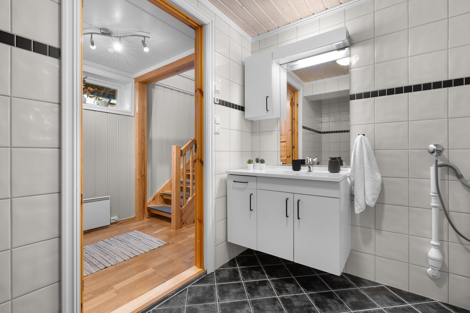 Lys baderomsinnredning med glatte fronter og heldekkende servant, speil med belysning og vegghengt skap over. Galleribilde