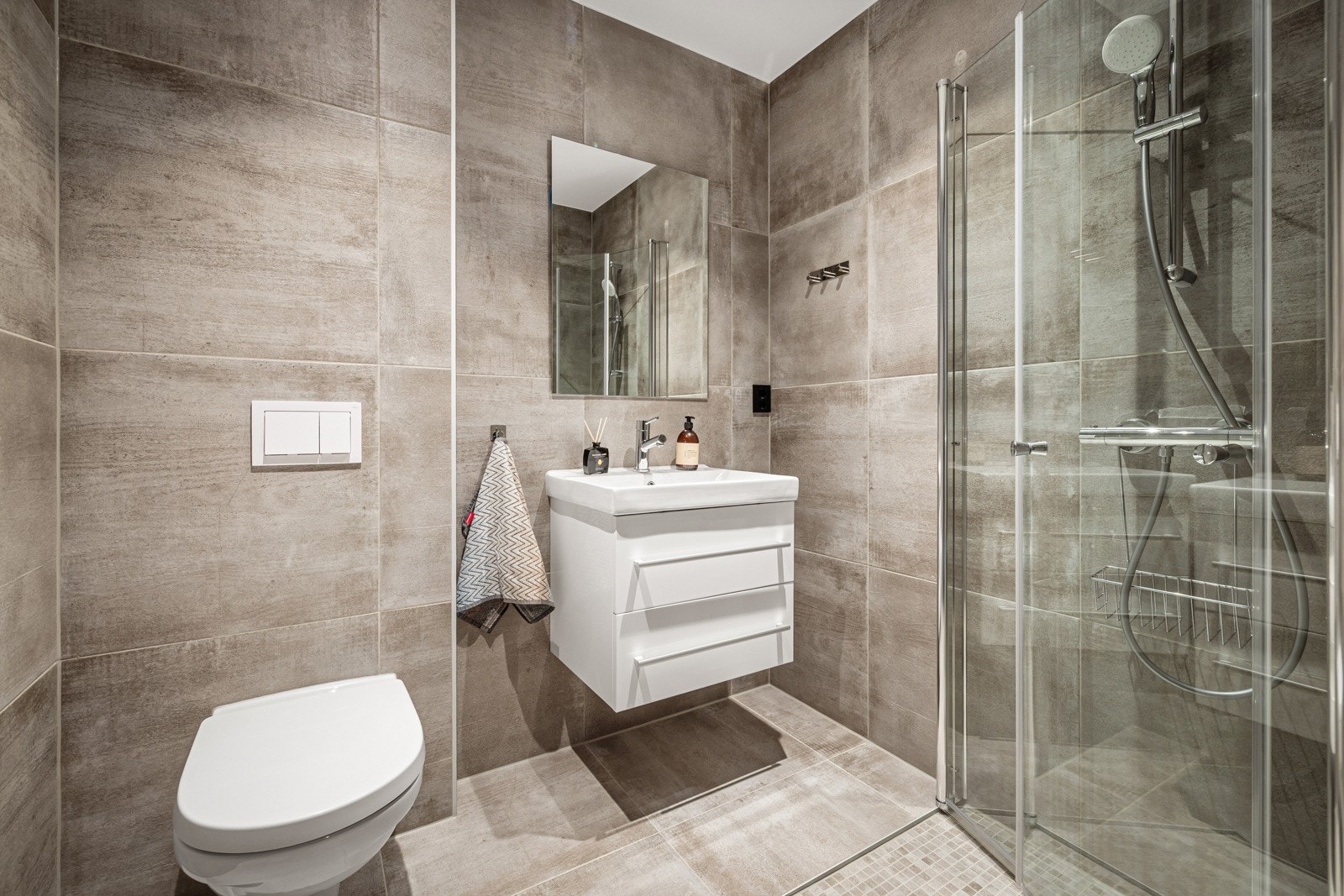 Badet i første etasje er innredert med servant i møbel, speil, vegghengt toalett og dusj med glassdører. Galleribilde