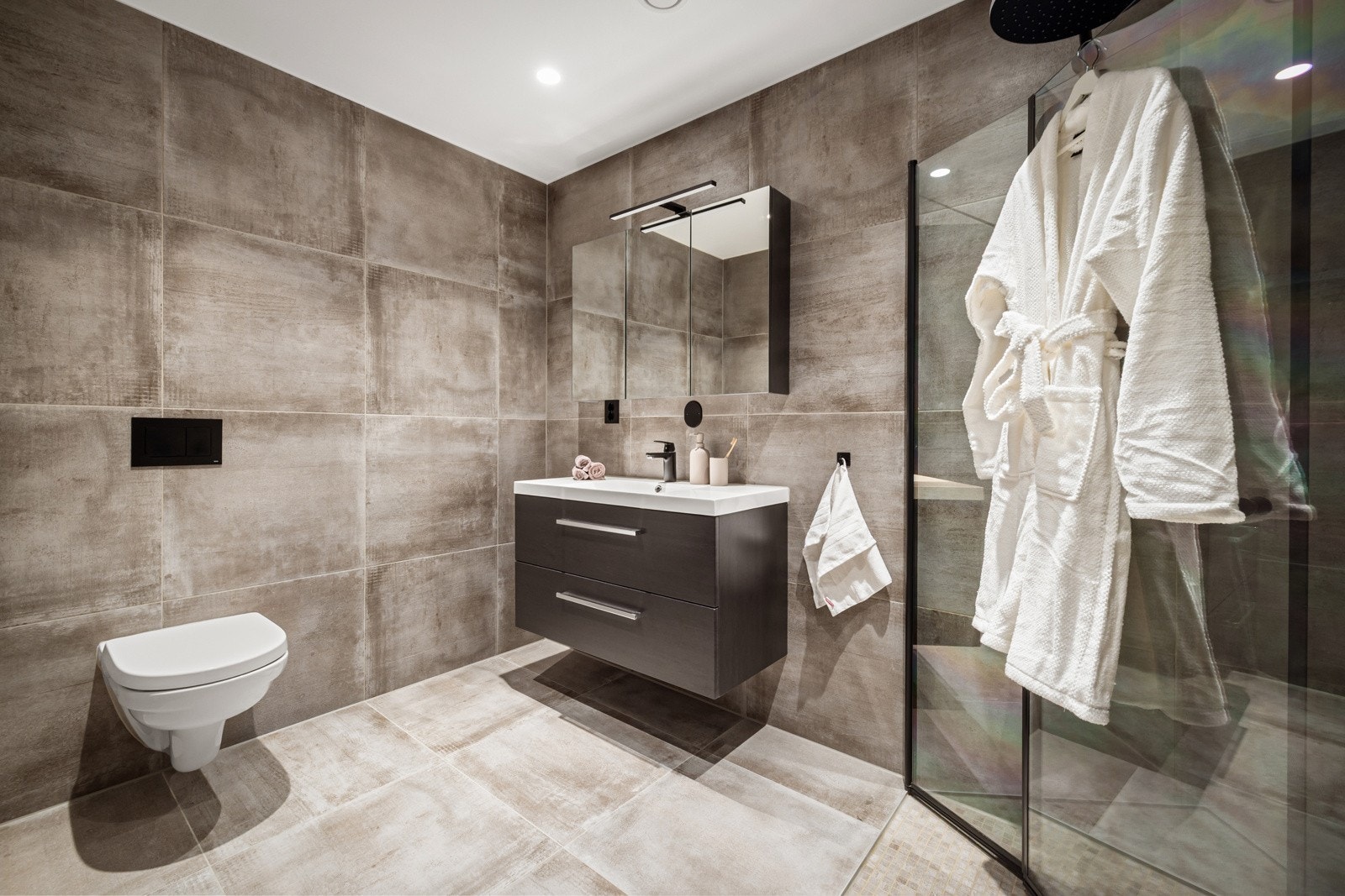 Badet i under etasjen er innredet med servant i møbel, speilskap med lys, vegghengt toalett og dusj med glassdører. Galleribilde