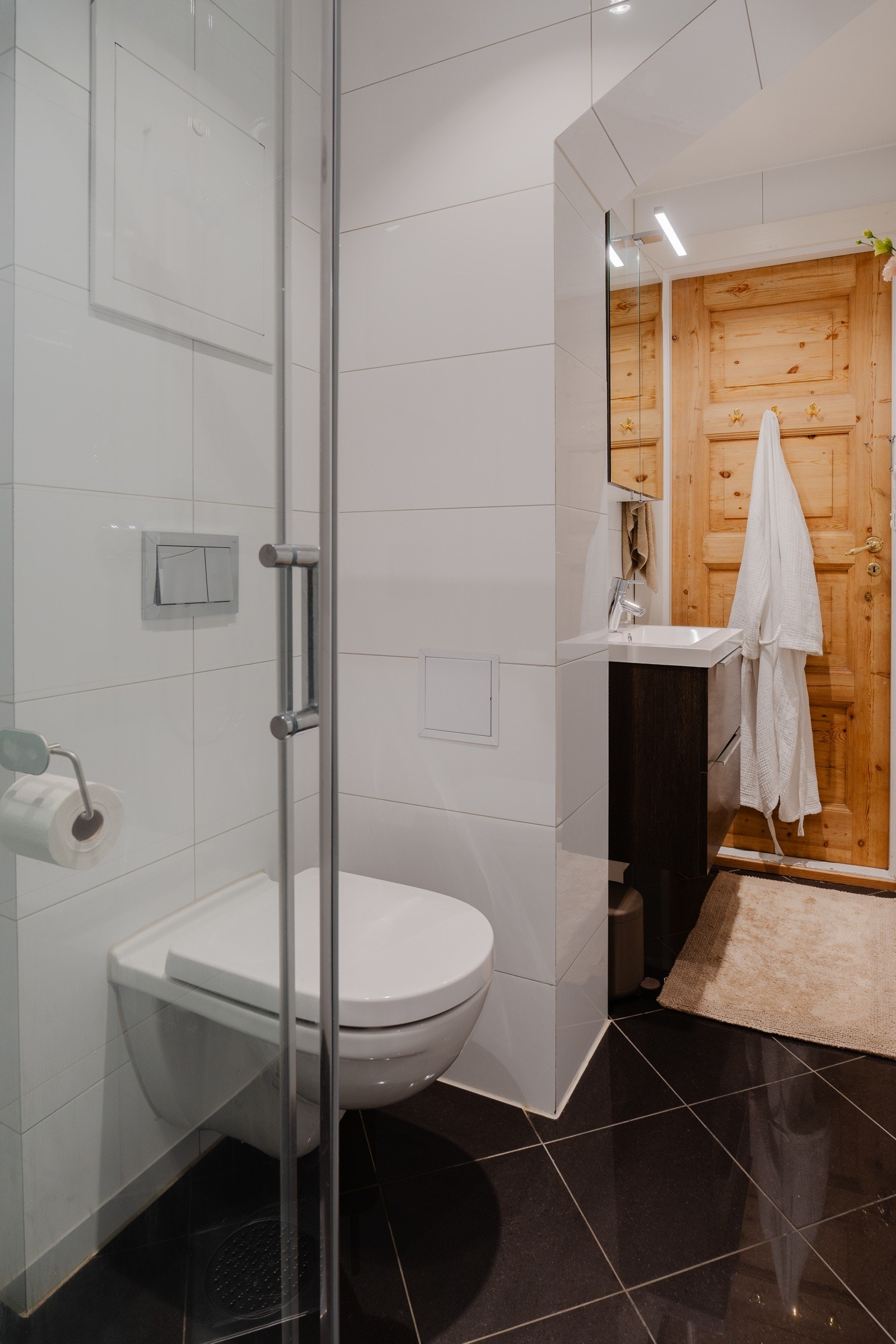 Rommet er utstyrt med et servantskap med speilskap og lys, et vegghengt toalett og en romslig dusjsone med skyvedør og regnfallsdusj. Galleribilde