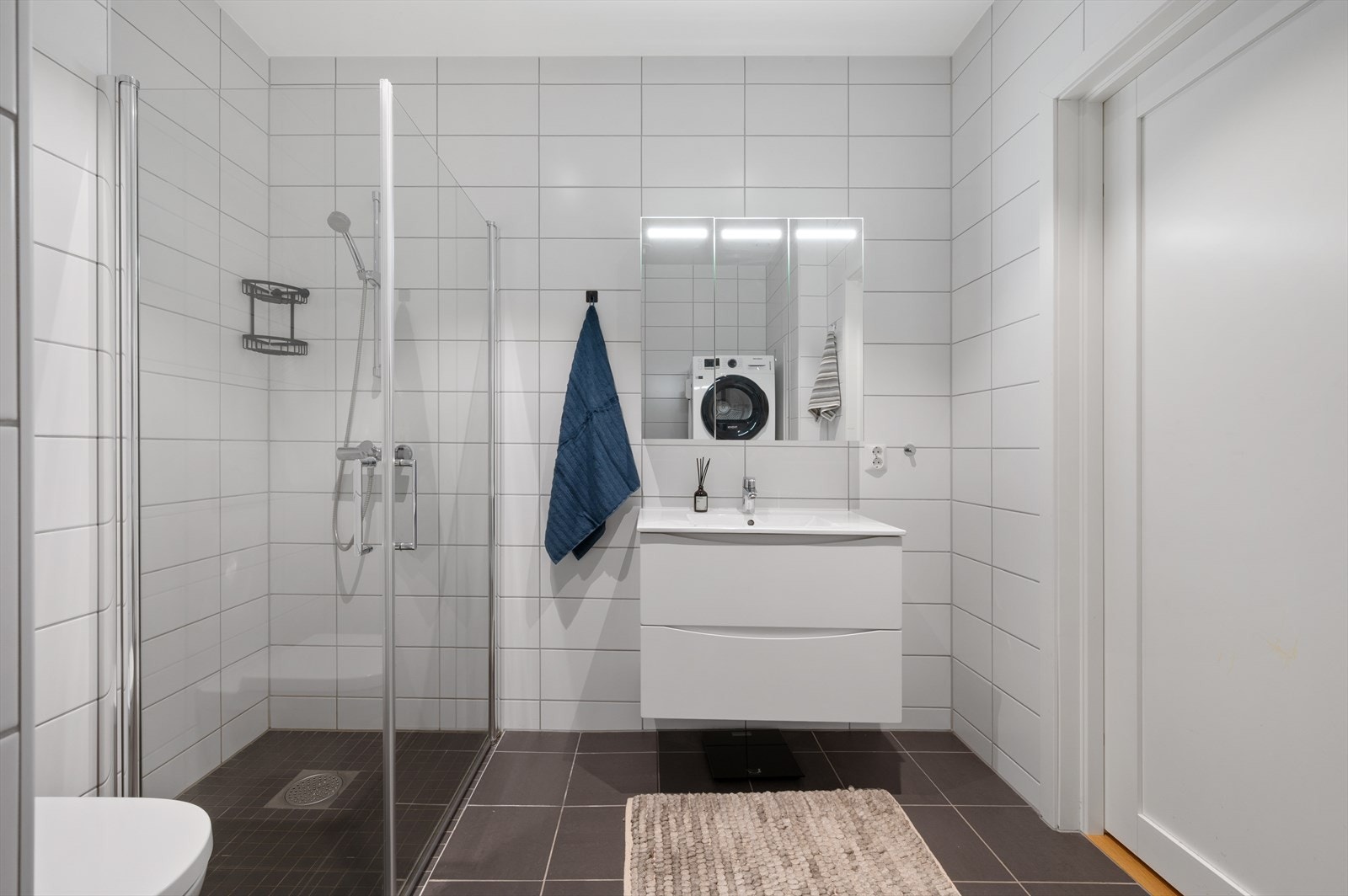 Badet er innredet med baderomsmøbel med heldekkende servant, speilskap m/ belysning, vegghengt toalett og dusj med glassdører. Galleribilde