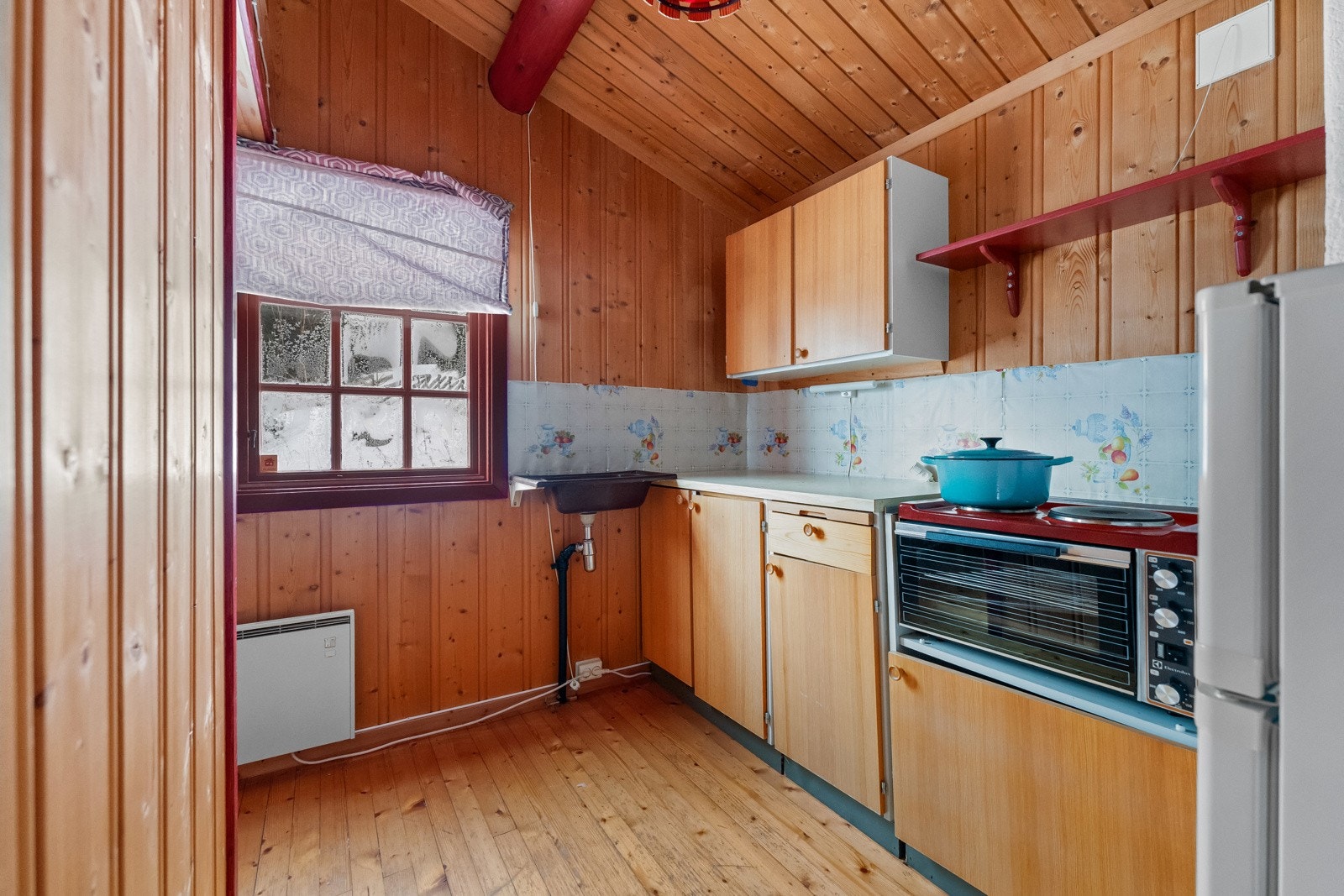 Enkel kjøkkeninnredning med slette fronter og laminert benkeplate. Utslagsvask er montert på vegg. Det store vinduet slipper inn godt med lys. Galleribilde