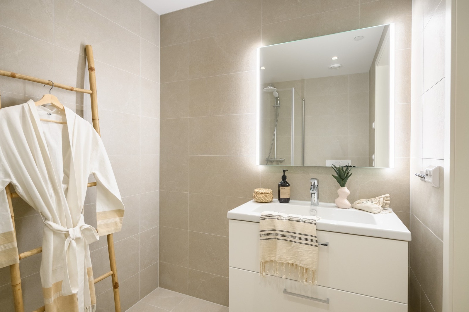 Delikat bad med hvit baderomsinnredning og speil med integrert belysning. Galleribilde