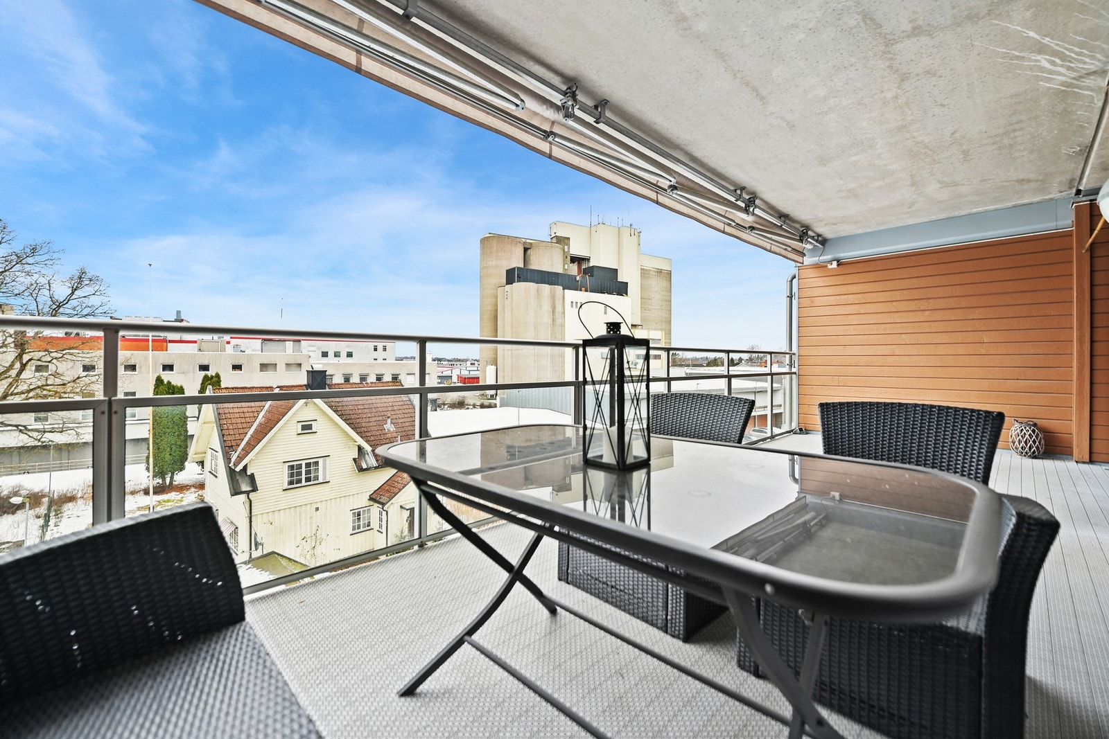 Stor, overbygd veranda med utsikt mot nærliggende bygninger og blå himmel. Galleribilde