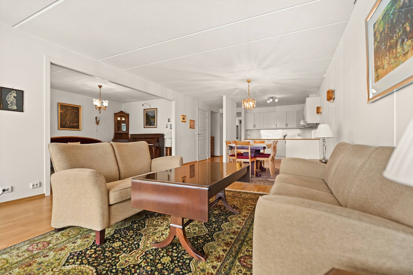 Åpen stue med lysinnslipp fra flere vinduer, og utsikt mot kjøkken. Galleribilde