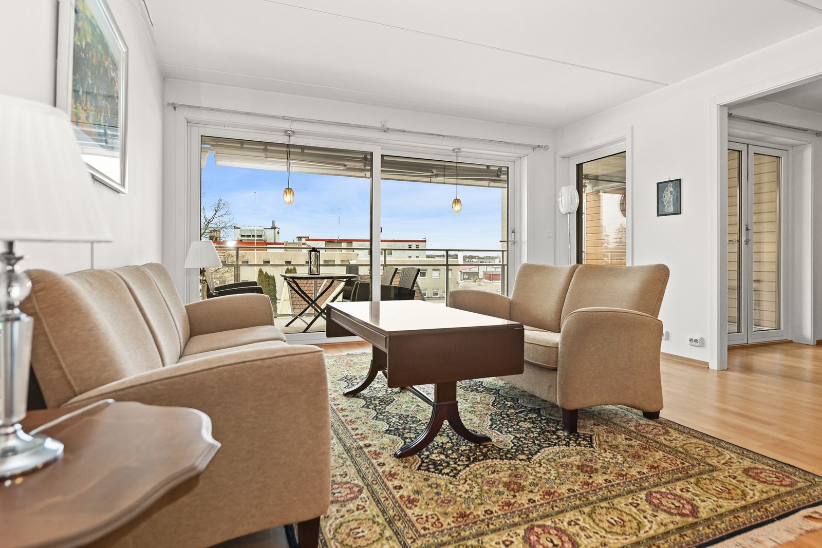 Lys stue med store vinduer og utgang til balkong. Vegger er malt hvite, og gulvet har parkett. Galleribilde