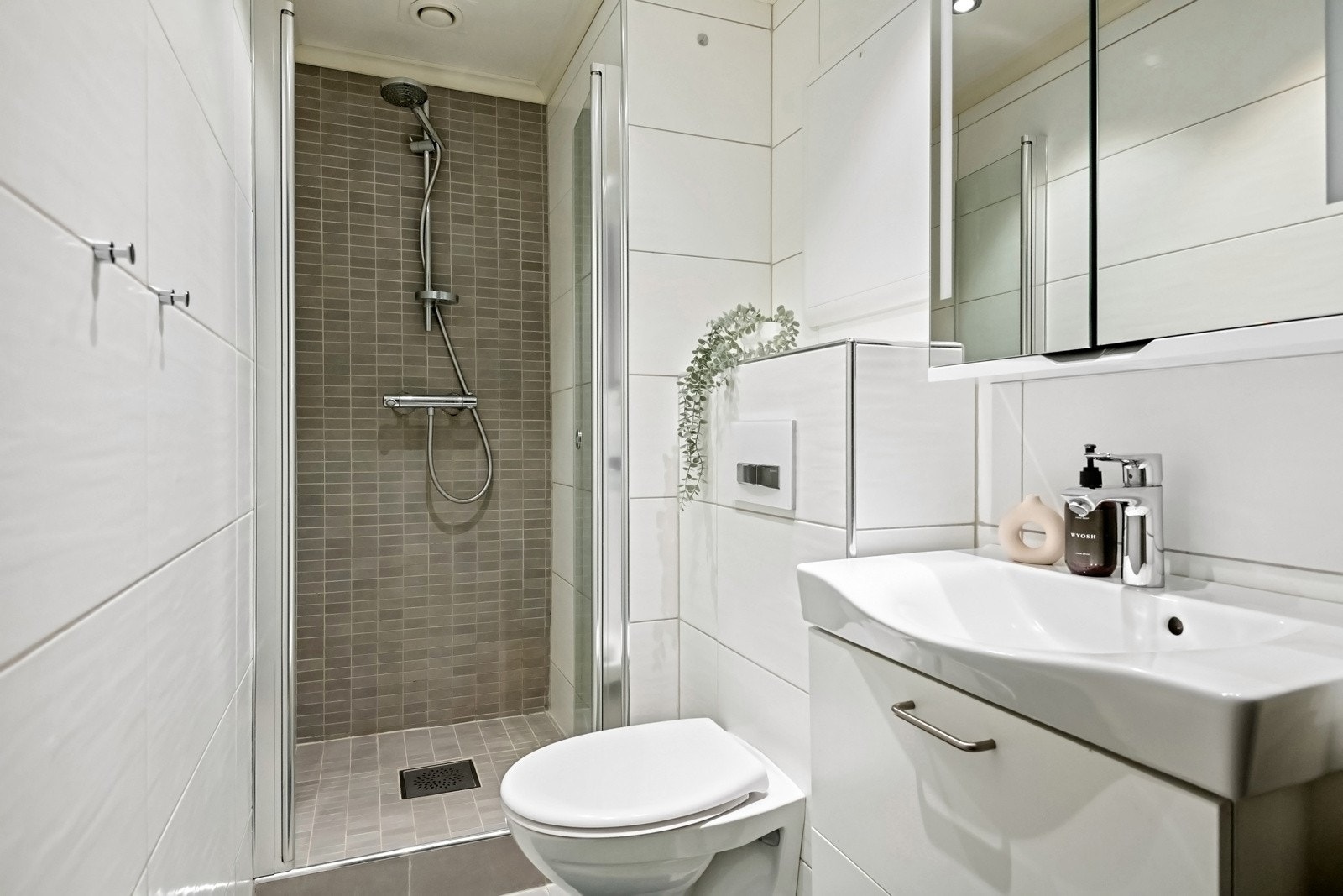 Dette badet er utstyrt med dusjnisje, servant og veggmontert toalett. Flislagte overflater og varmekabler i gulvet gir et praktisk og helhetlig uttrykk. Galleribilde