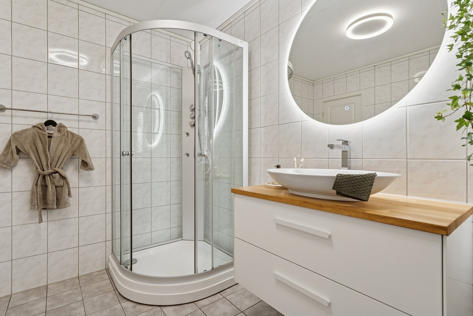 Badet har et praktisk dusjkabinett og fin innredning med servant og lyssatt speil over. Galleribilde