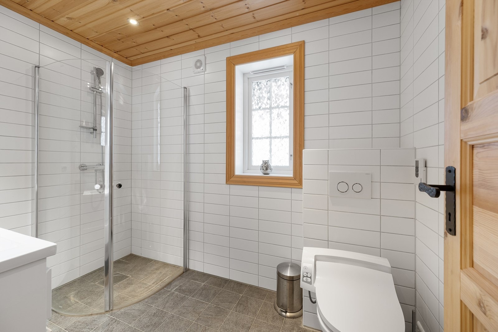 Badet har flislagt gulv med gulvvarme, fliser på vegger, innfelte downlights, vegghengt toalett og innfellbare dusjdører. Galleribilde