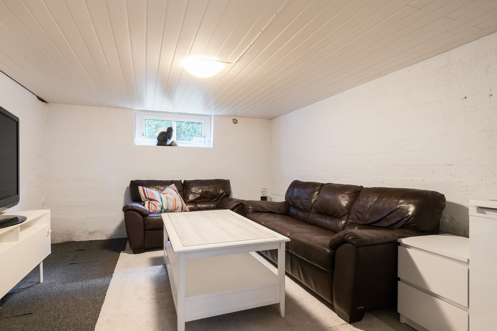 I kjelleren er et rom innredet som en kjellerstue med plass til sofagruppe og tv, perfekt som ekstra oppholdsrom. Galleribilde