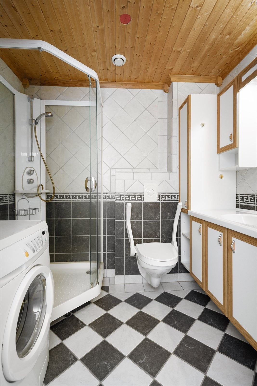 Helfliset bad innredet med veggmontert toalett, dusjkabinett og servantinnredning med skap og speil. Det er opplegg for vaskemaskin. Galleribilde