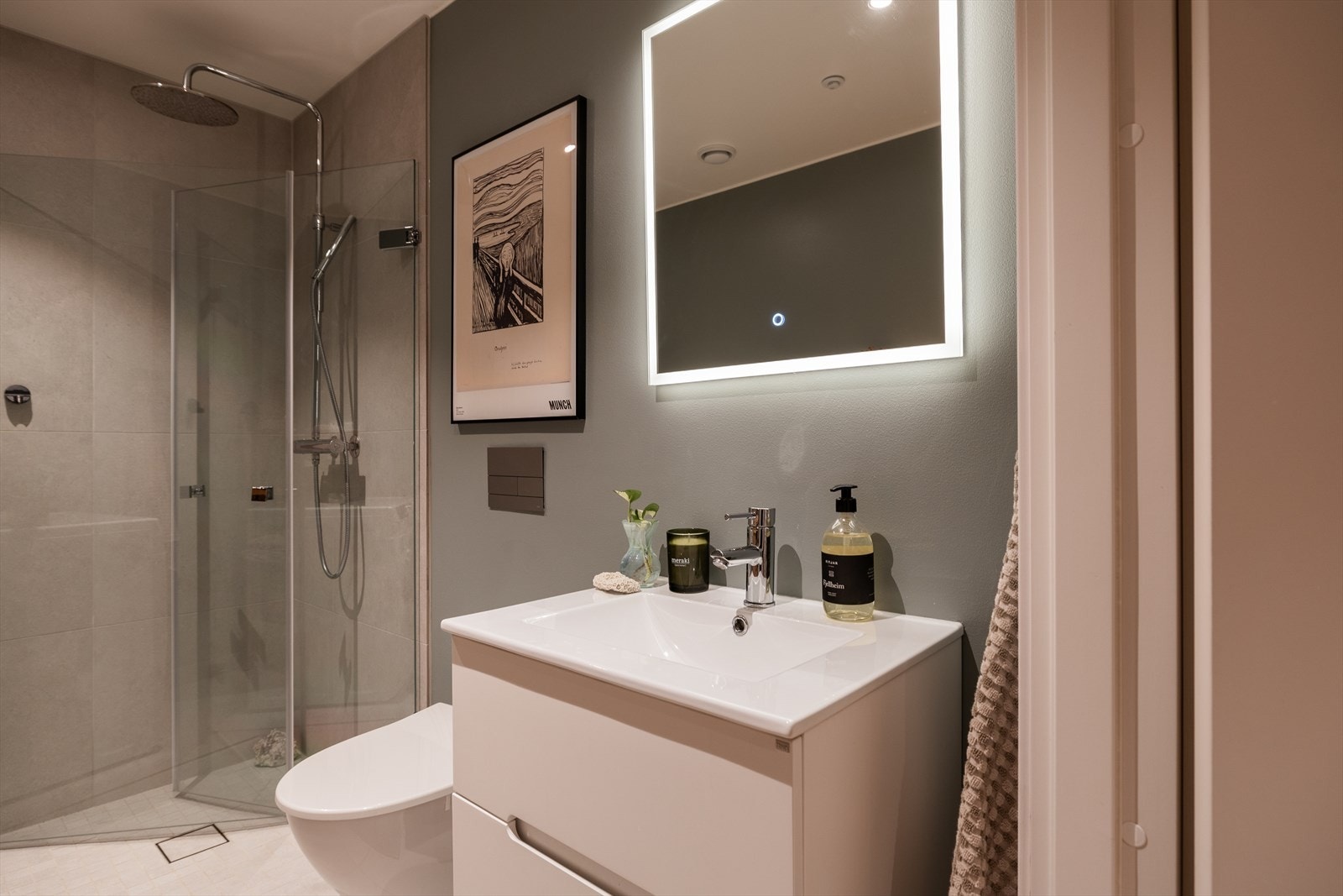 Badet er ellers utstyrt med baderomsrinnredning, speil, dusjhjørne med innfellbare glassdører, mekanisk avtrekk, rørfordelingsskap og veggmontert wc. Galleribilde