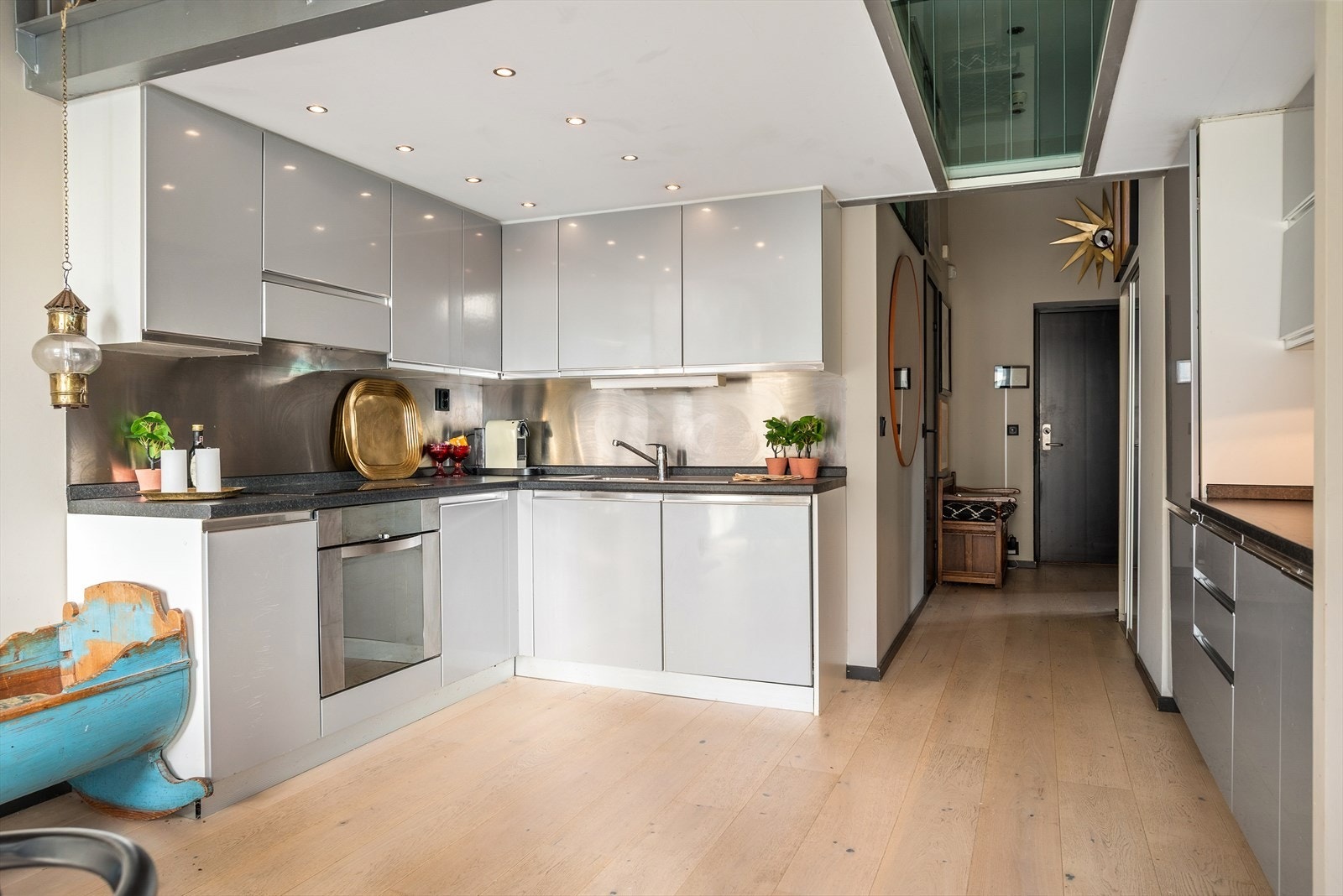 Kjøkkenet har stilrene glatte fronter, laminat benkeplate med nedfelt kum i rustfritt stål og stålplater på vegg over benk. Galleribilde